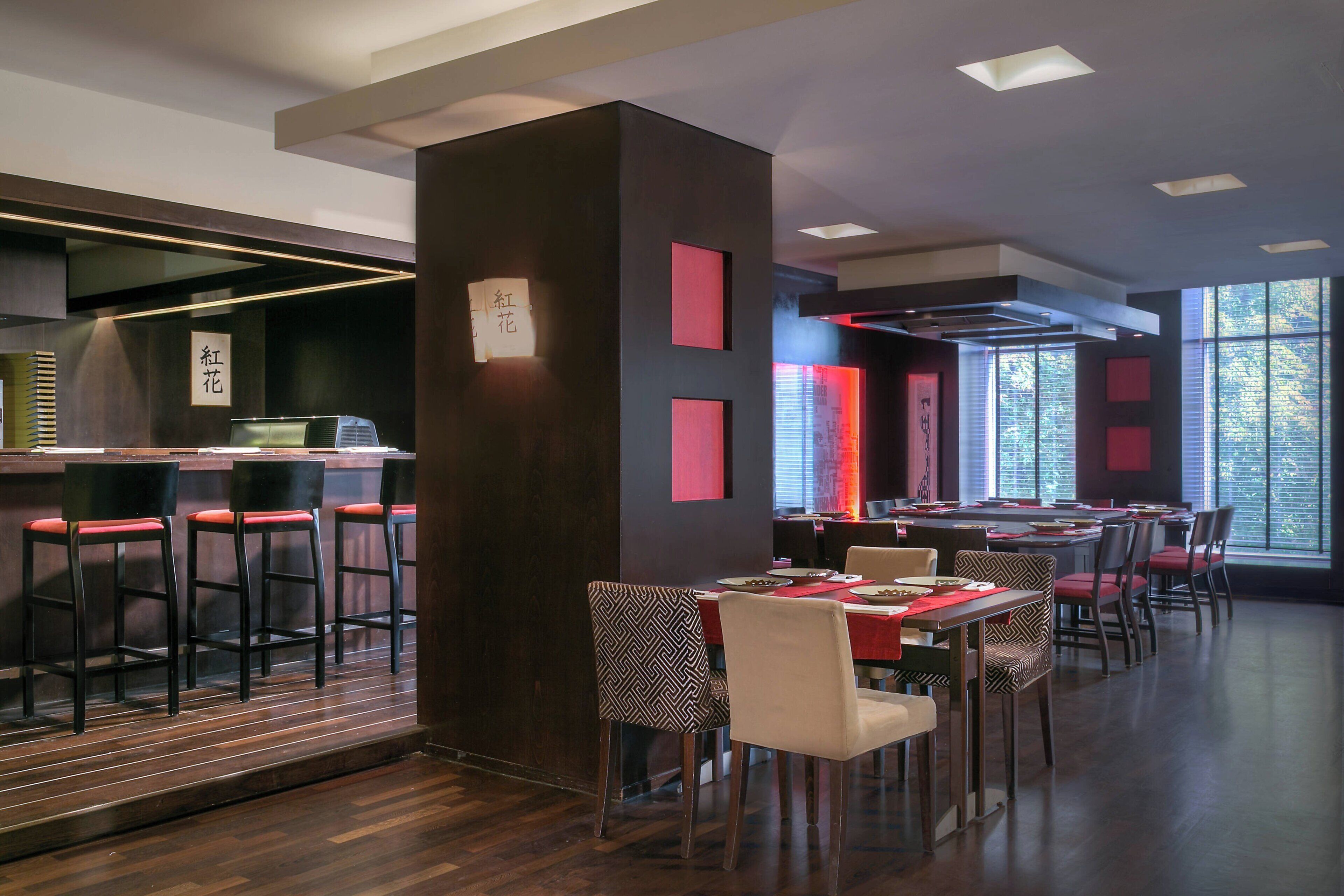 A modern restaurant interior with bar seating, tables, and a view through large windows.