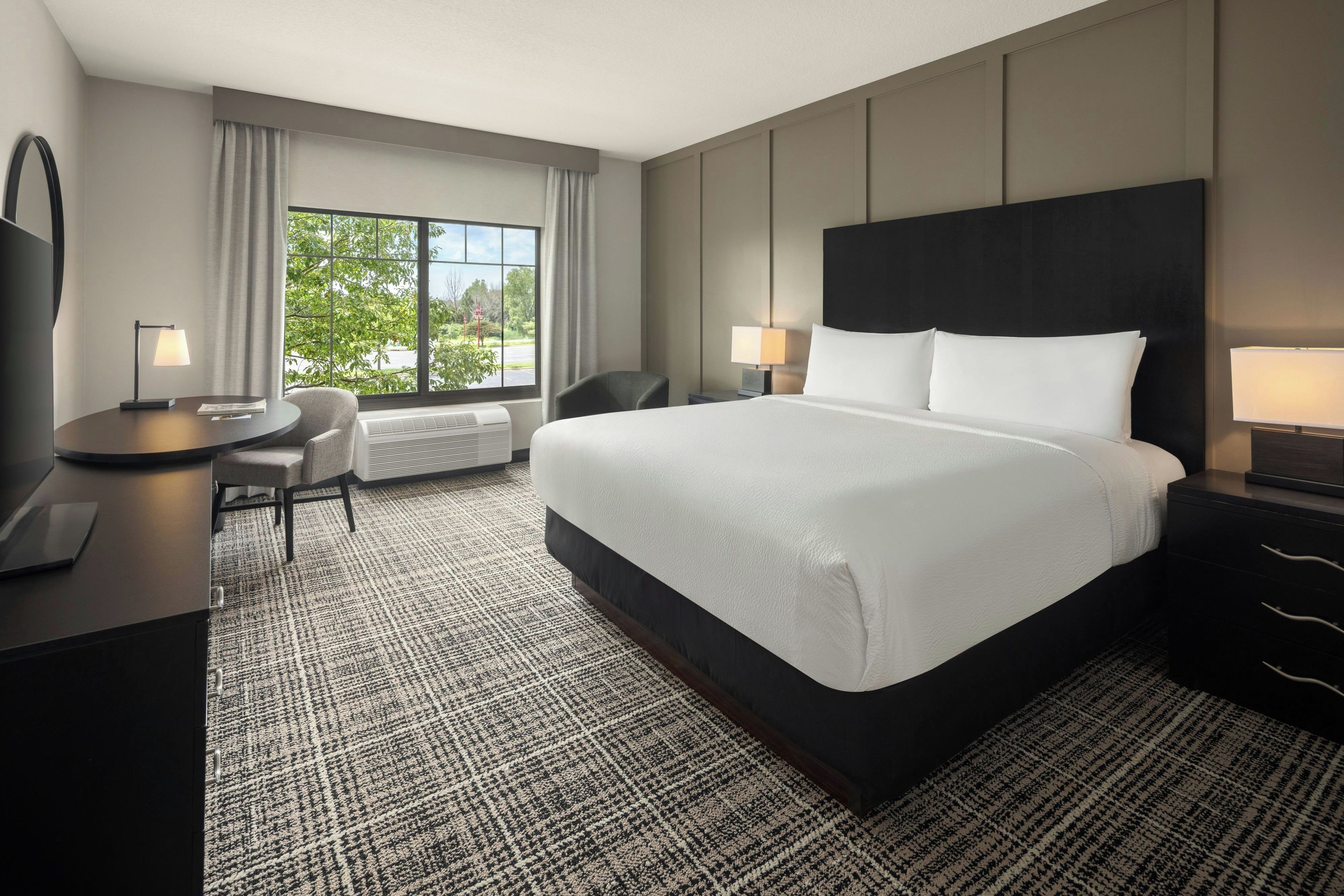 Una habitación de hotel con una cama grande, un escritorio, una silla y vistas al exterior.