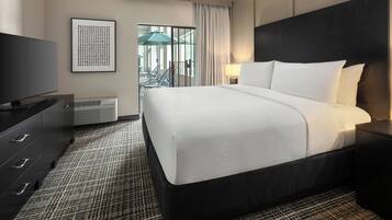 A hotel room with a large bed, a television, a dresser, and a view of the outdoor area.