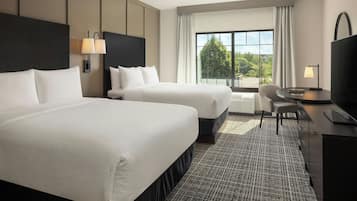 A hotel room with two beds, a desk, a chair, and a large window with a view.
