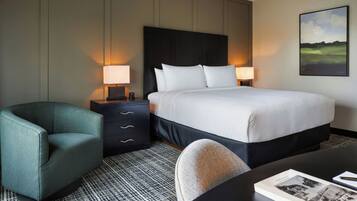 Habitación de hotel con una cama, dos lámparas de noche, una silla, un escritorio y un cuadro en la pared.