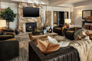 Una sala de estar con chimenea de piedra, sofás de cuero, un televisor de pantalla plana y una mesa de centro con objetos decorativos.