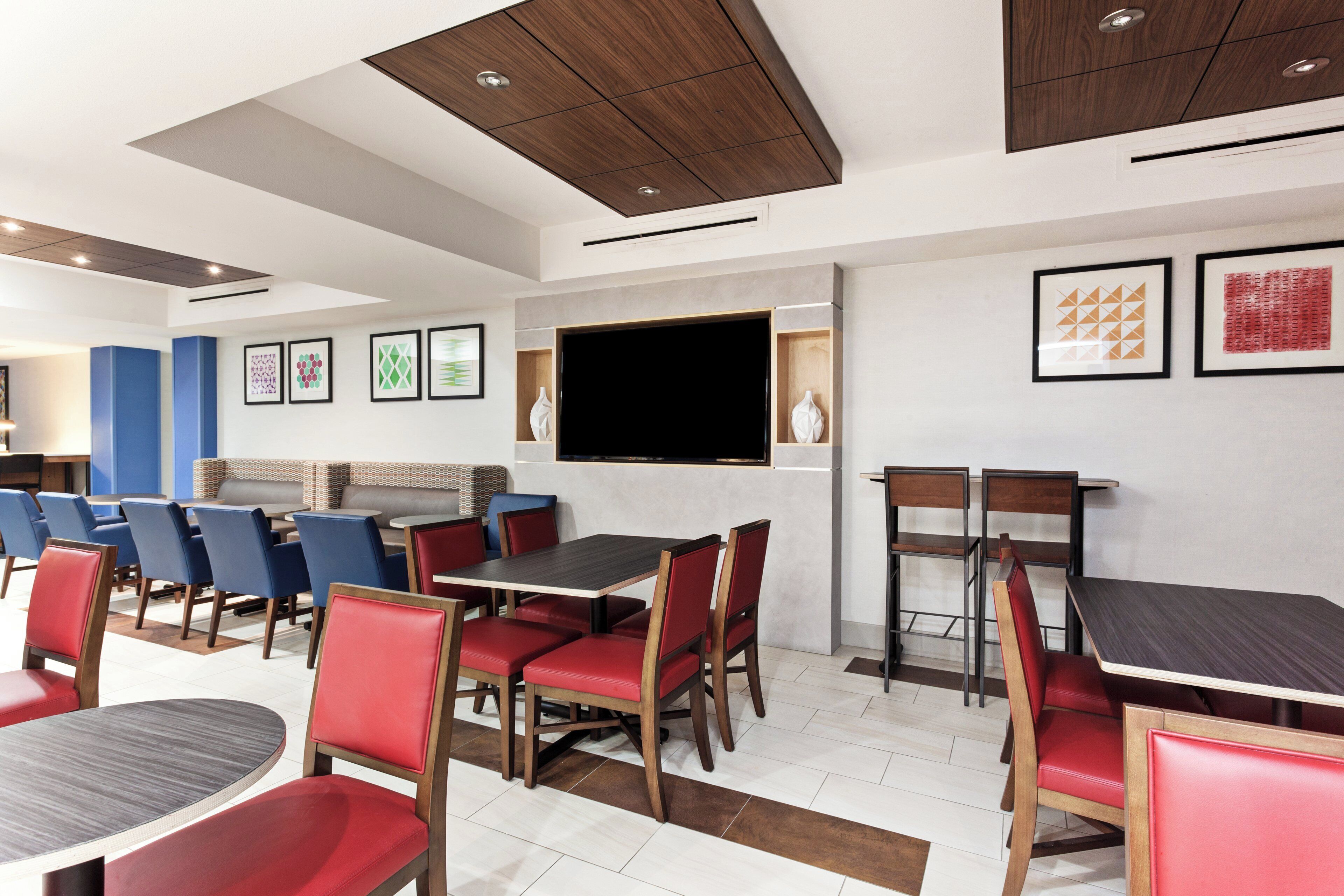 Un espace repas moderne, doté de plusieurs tables et chaises, d’un téléviseur à écran plat fixé au mur et d’œuvres d’art encadrées qui décorent les murs.