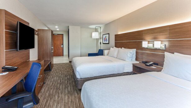 Habitación de hotel con dos camas, un escritorio con silla, televisor y mesita de noche con lámpara.