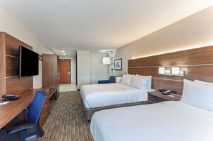 Habitación de hotel con dos camas, un escritorio con silla, televisión y una mesita de noche con lámpara.