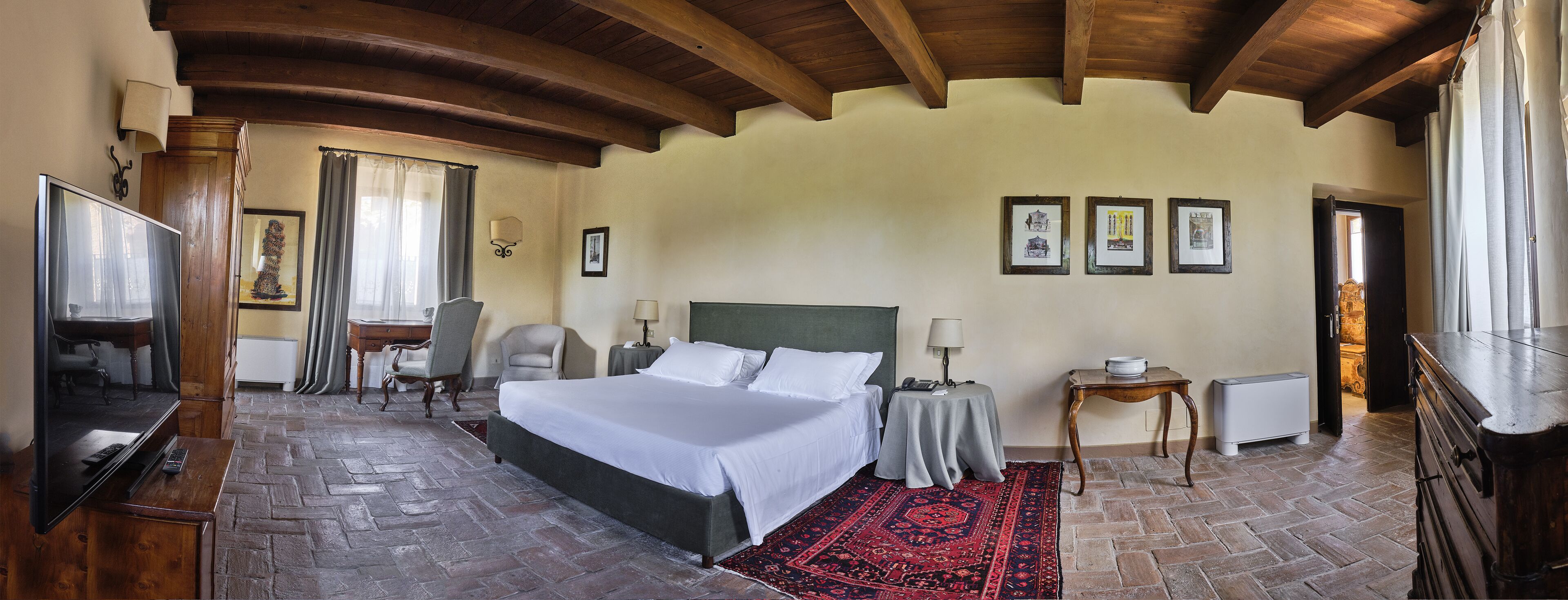 A hotel room with a large bed, a desk, a chair, a TV, and a red rug.