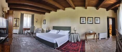 A hotel room with a large bed, a desk, a chair, a TV, and a red rug.