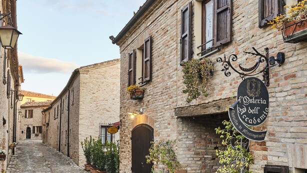 Una strada acciottolata con un edificio che presenta un cartello con scritto 'Osteria dell'Accademia'.
