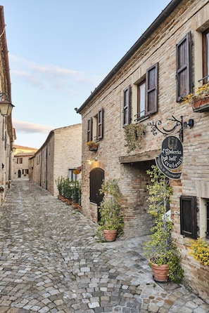 A cobblestone street with a building featuring a sign for 'Osteria dell'Accademia'. - Palazzo Viviani Castello di Montegridolfo  (Montegridolfo)