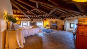 Un'ampia camera da letto con un letto grande, un angolo salotto con una poltrona e un tavolino, e una televisione.