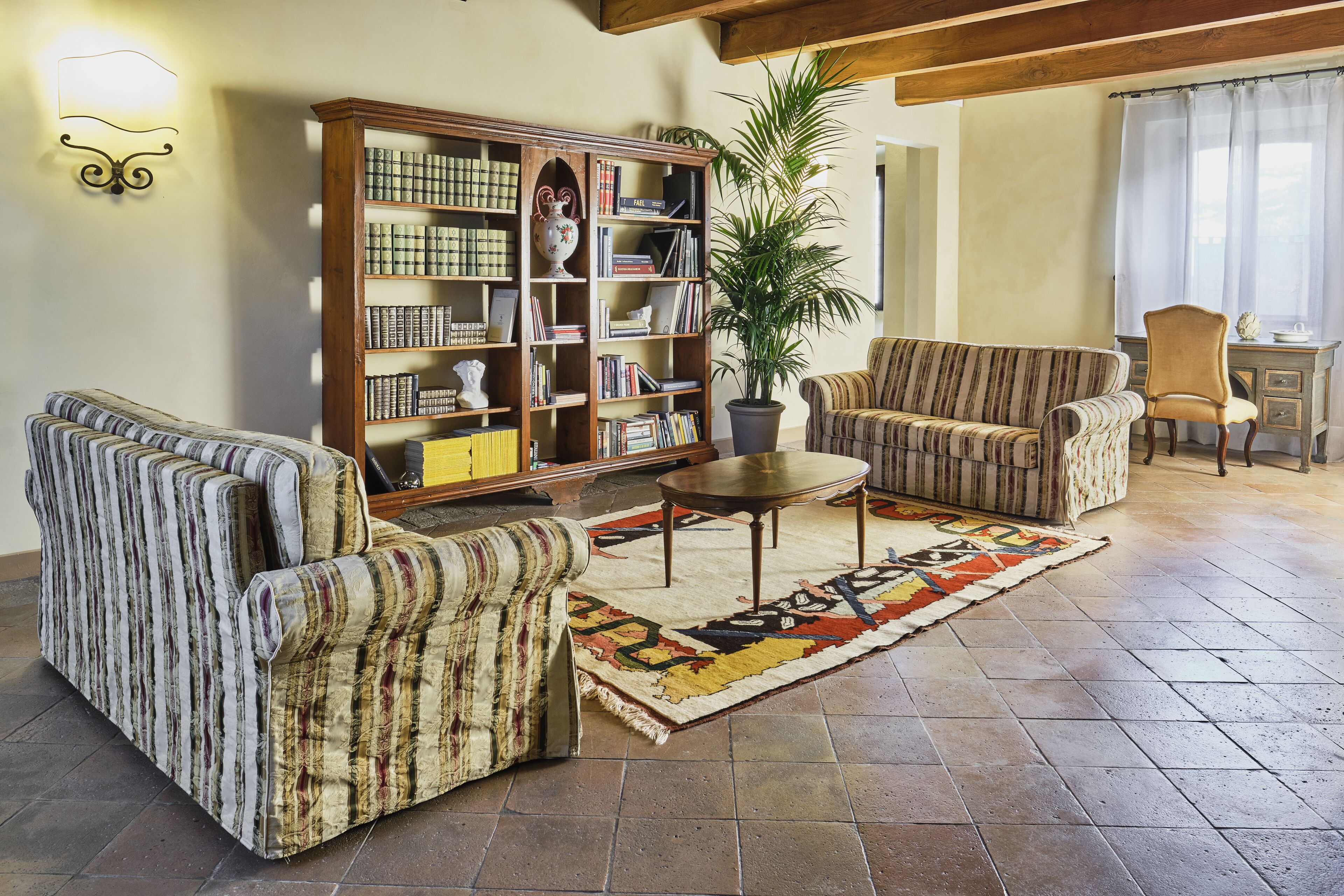 A cozy living room with striped armchairs, a sofa, a bookshelf, and a potted plant.