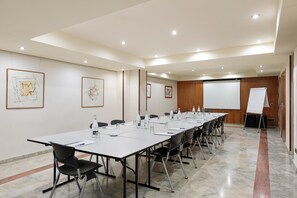 Un salón de conferencias con una larga mesa, sillas, una pantalla de proyector y obras de arte enmarcadas en las paredes.