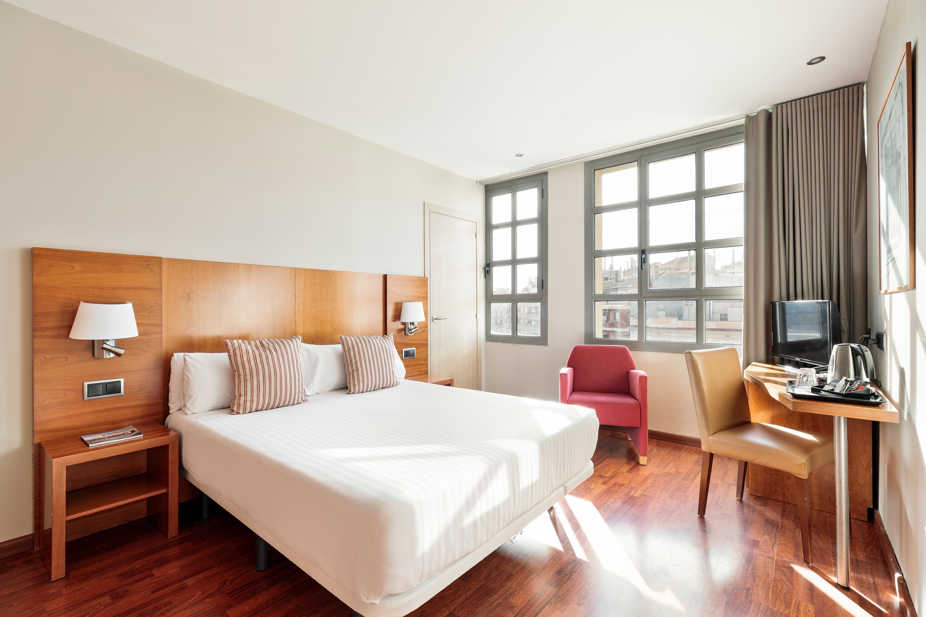 Habitación de hotel con una cama grande, un escritorio con silla, televisión y ventana con cortinas.