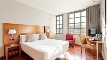 Habitación de hotel con una cama grande, un escritorio con silla, televisión y ventana con cortinas.