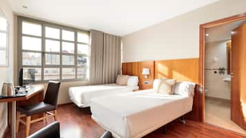 Ein Hotelzimmer mit zwei Betten, einem Schreibtisch, einem Stuhl, einem Fenster mit Vorhängen und einem Holzkopfteil.
