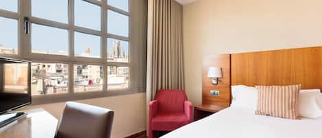 Habitación de hotel con cama, escritorio con computadora, silla, televisión y ventana con cortinas.