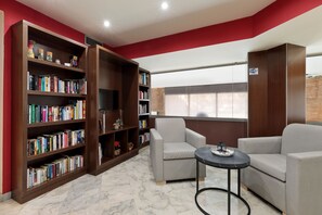 A modern reading area with a large bookshelf, two grey sofas, and a small table. - Hotel Best Aranea (Barcelona)