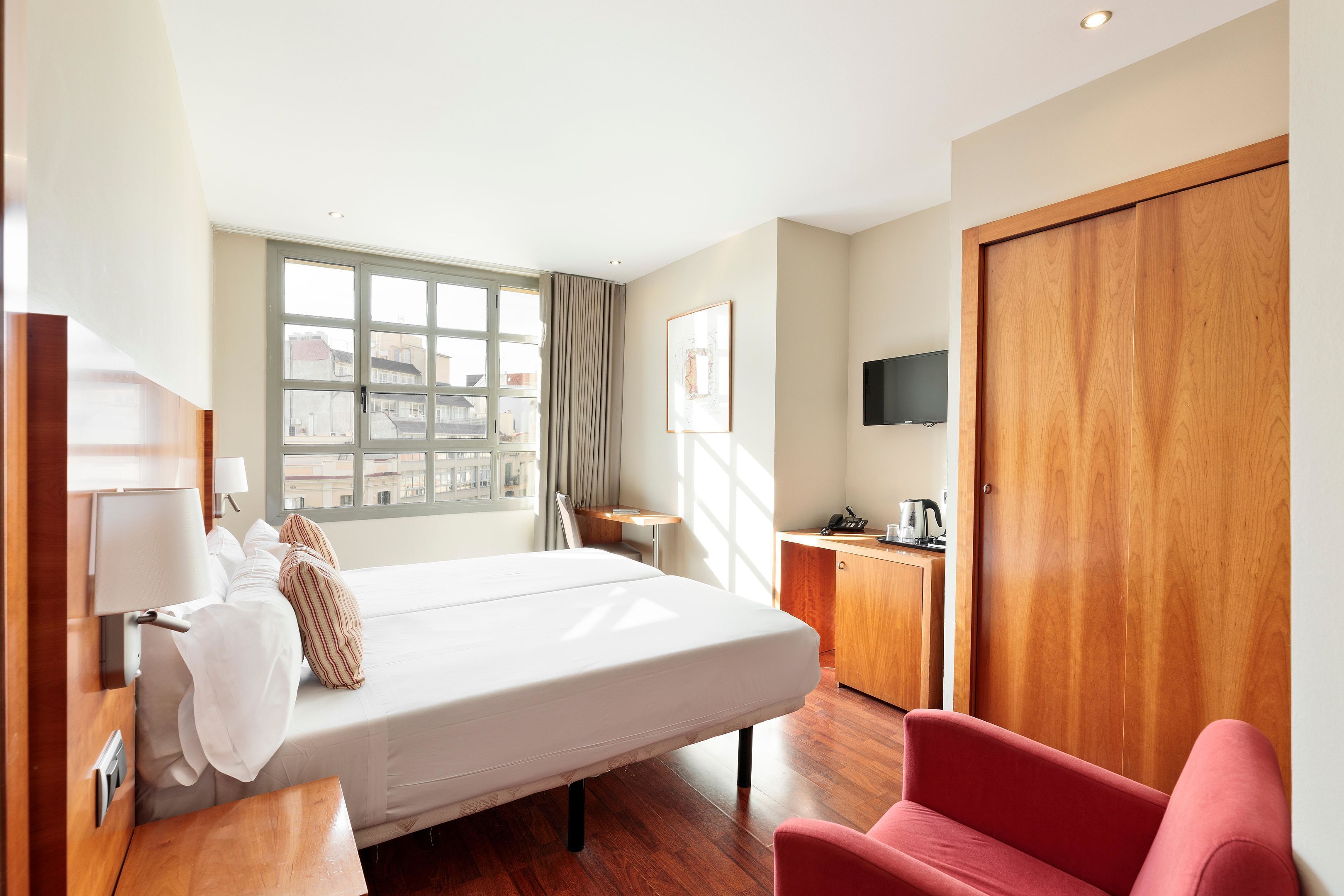 Una habitación de hotel con una cama, un escritorio, una silla, un televisor y una ventana con cortinas.
