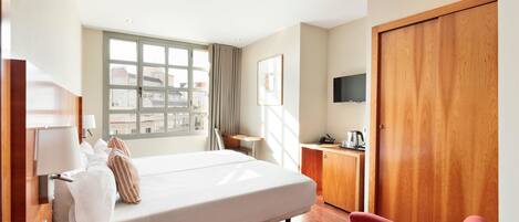 Una habitación de hotel con una cama, un escritorio, una silla, un televisor y una ventana con cortinas.
