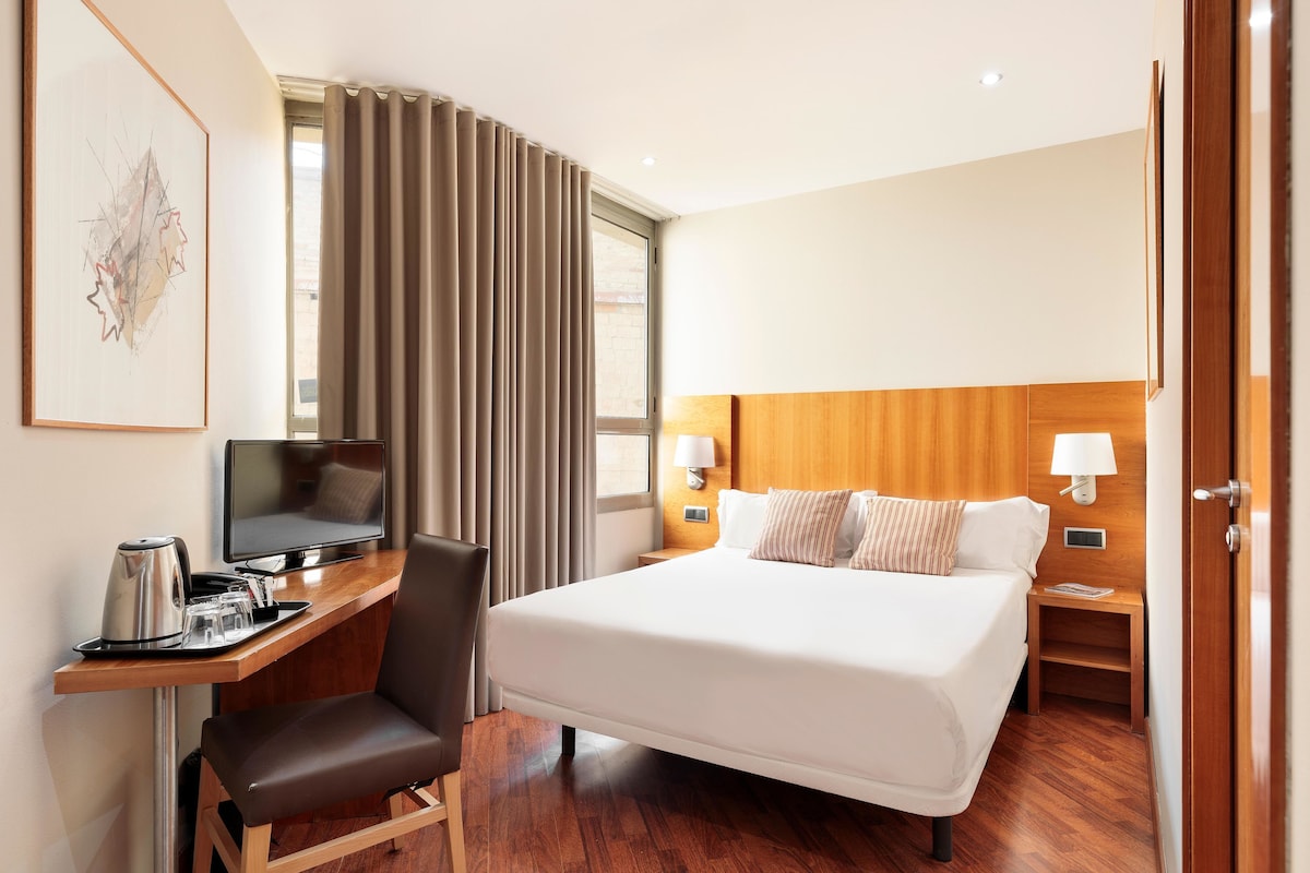 A hotel room with a bed, desk, chair, and a TV.