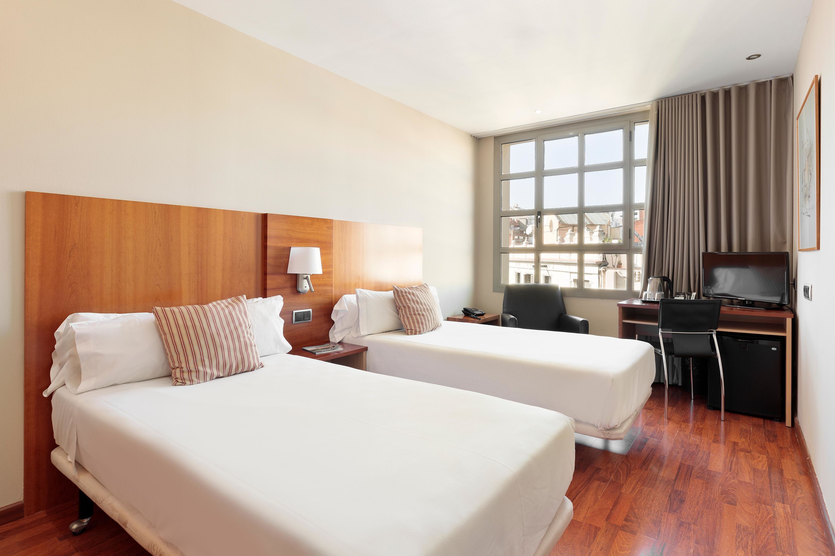 Habitación de hotel con dos camas, un escritorio, una silla, un televisor y una ventana con cortinas.