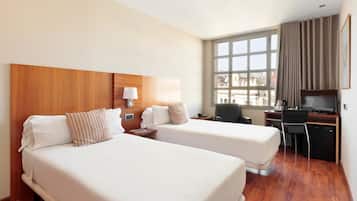 Habitación de hotel con dos camas, un escritorio, una silla, un televisor y una ventana con cortinas.