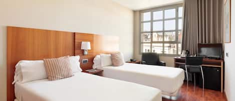 A hotel room with two beds, a desk, a chair, a television, and a window with curtains.