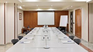A conference room with a long table, chairs, a projector screen, and a whiteboard.