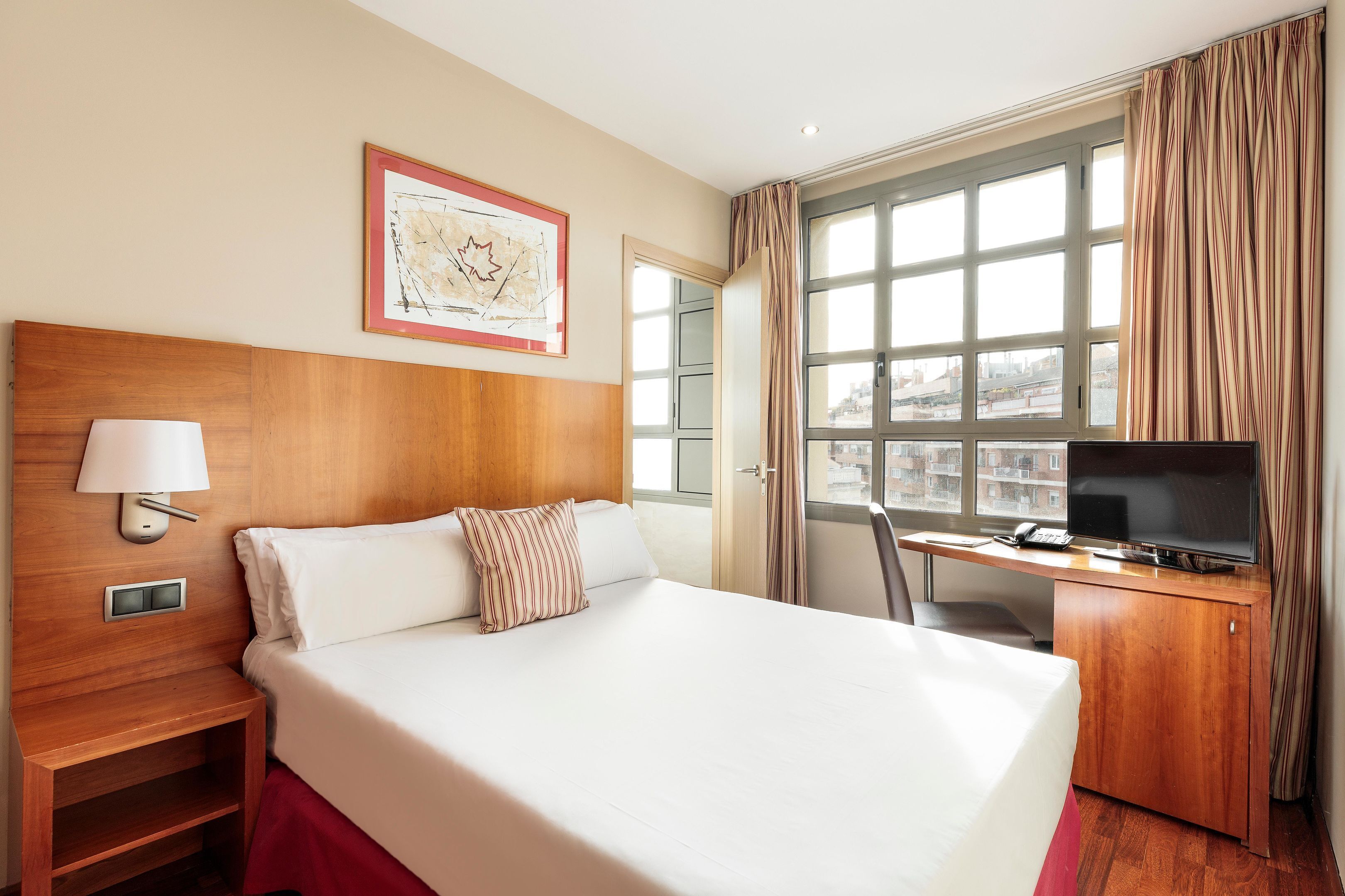 Ein Hotelzimmer mit einem großen Bett, einem Schreibtisch mit Fernseher, einem Fenster mit Vorhängen und einer gerahmten Karte an der Wand.