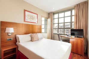 Una habitación de hotel con una cama grande, un escritorio con televisor, una ventana con cortinas y un mapa enmarcado en la pared.