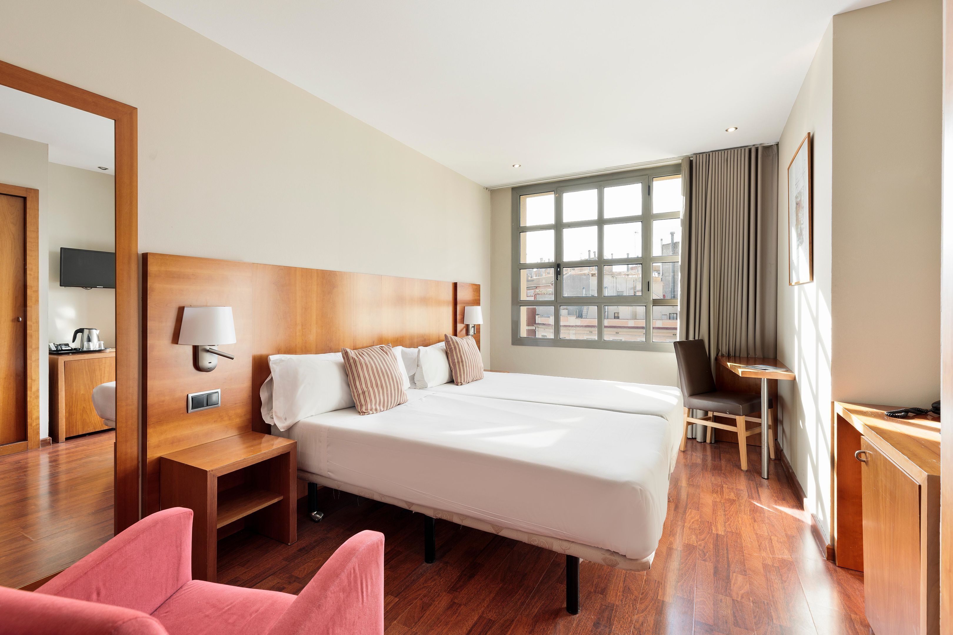 Una habitación de hotel con una cama grande, mesitas de noche, un escritorio, una silla y una ventana con cortinas.