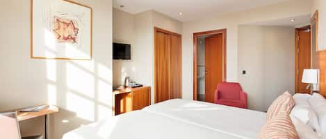 A hotel room with a large bed, a desk with a chair, a TV, and a wooden wardrobe.