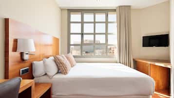 Une chambre d’hôtel avec un grand lit, un bureau, une chaise, une télévision et une fenêtre donnant sur la ville.
