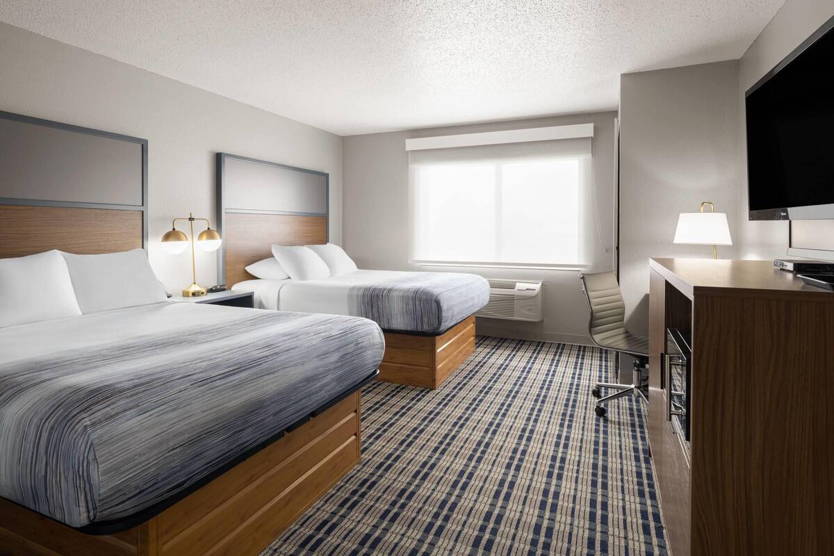 A hotel room with two beds, a desk, a TV, and a large window.