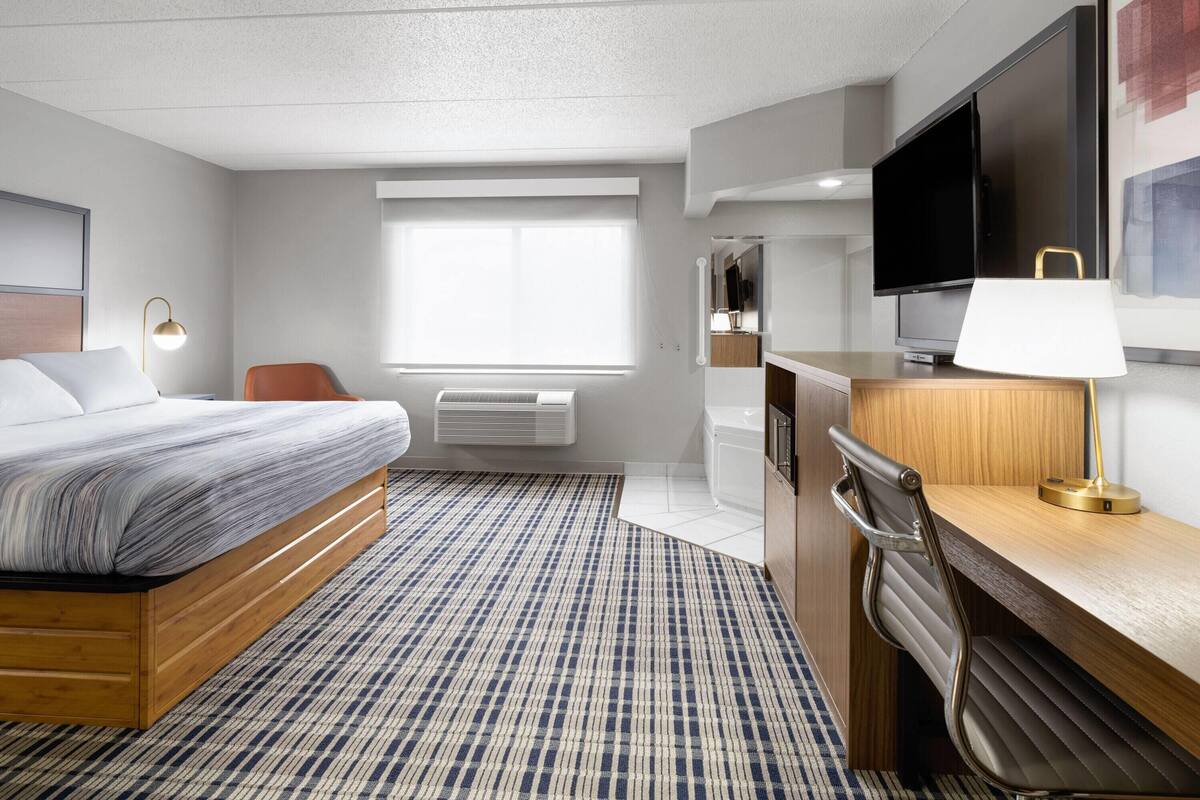 A hotel room with a bed, desk, TV, and a window.