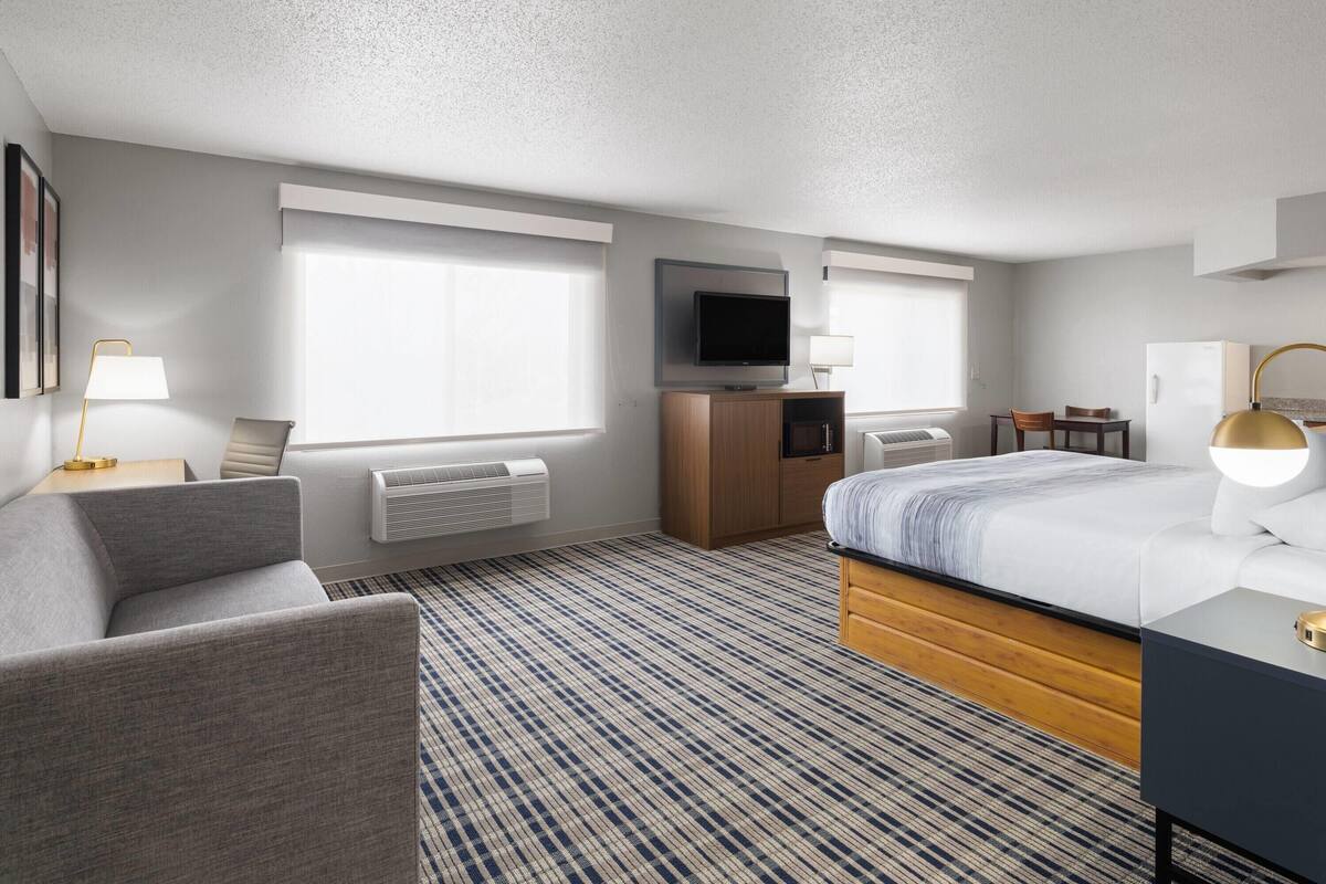 A hotel room with a bed, a desk, a chair, a TV, and a window.