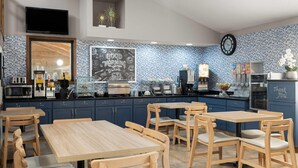 A modern kitchen with dark blue cabinets, wooden tables, and chairs. There is a chalkboard with 'Good Morning' written on it, and a clock on the wall. - AmericInn by Wyndham Muscatine (Muscatine)