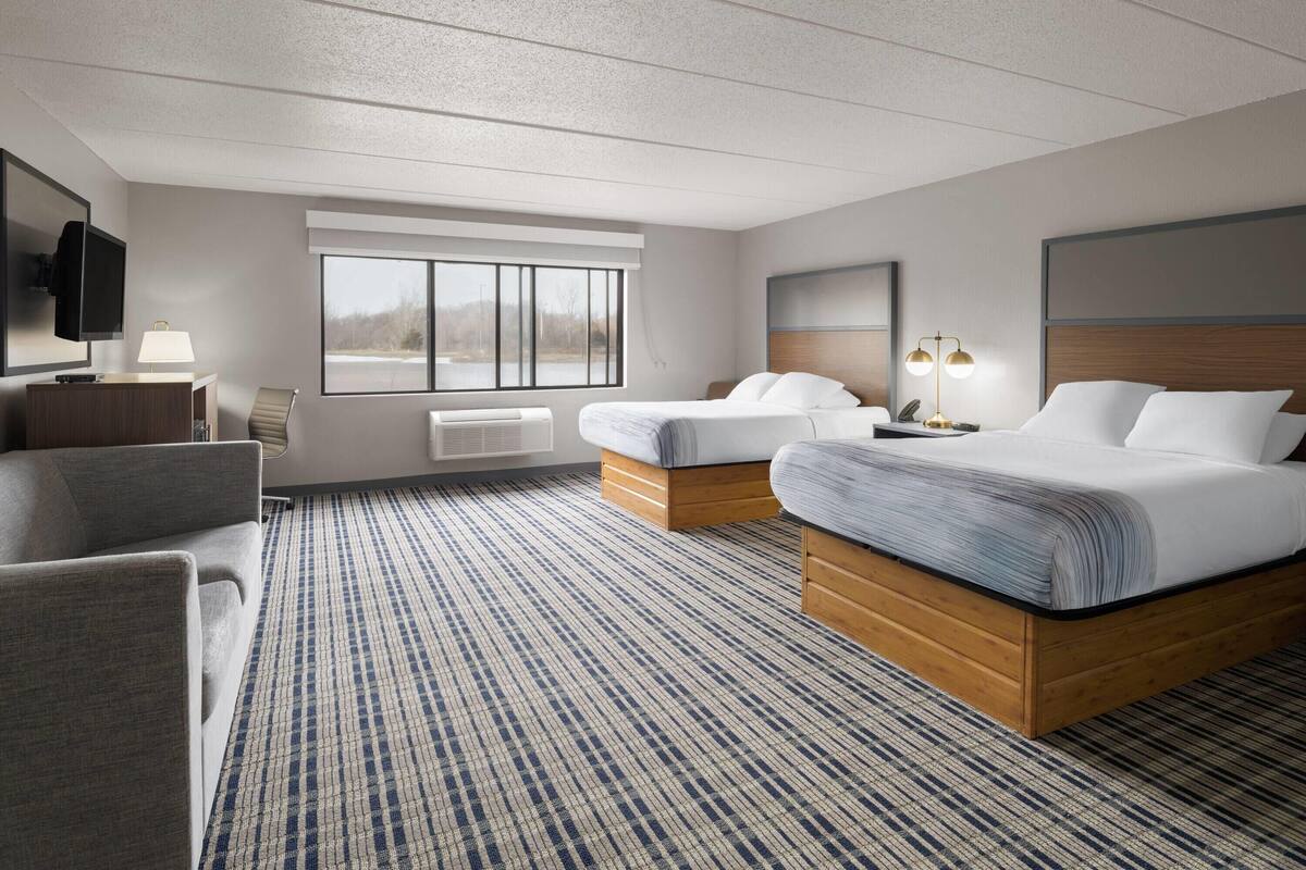 A hotel room with a large bed, a smaller bed, a sofa, a TV, and a window with a view.