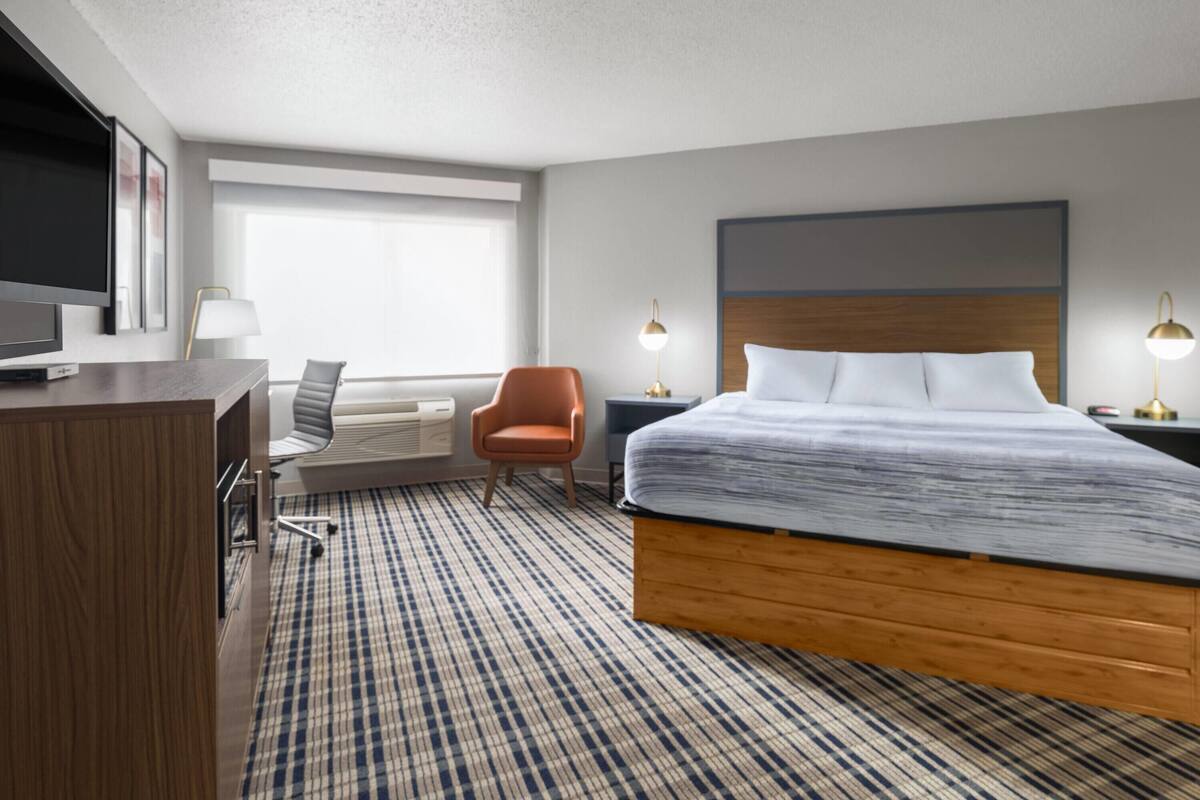 A hotel room with a large bed, a desk with a TV, a chair, and two bedside lamps.