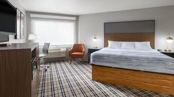 A hotel room with a large bed, a desk with a TV, a chair, and two bedside lamps.