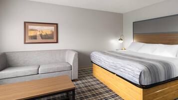 A hotel room with a bed, a gray sofa, a wooden table, and a framed picture on the wall.