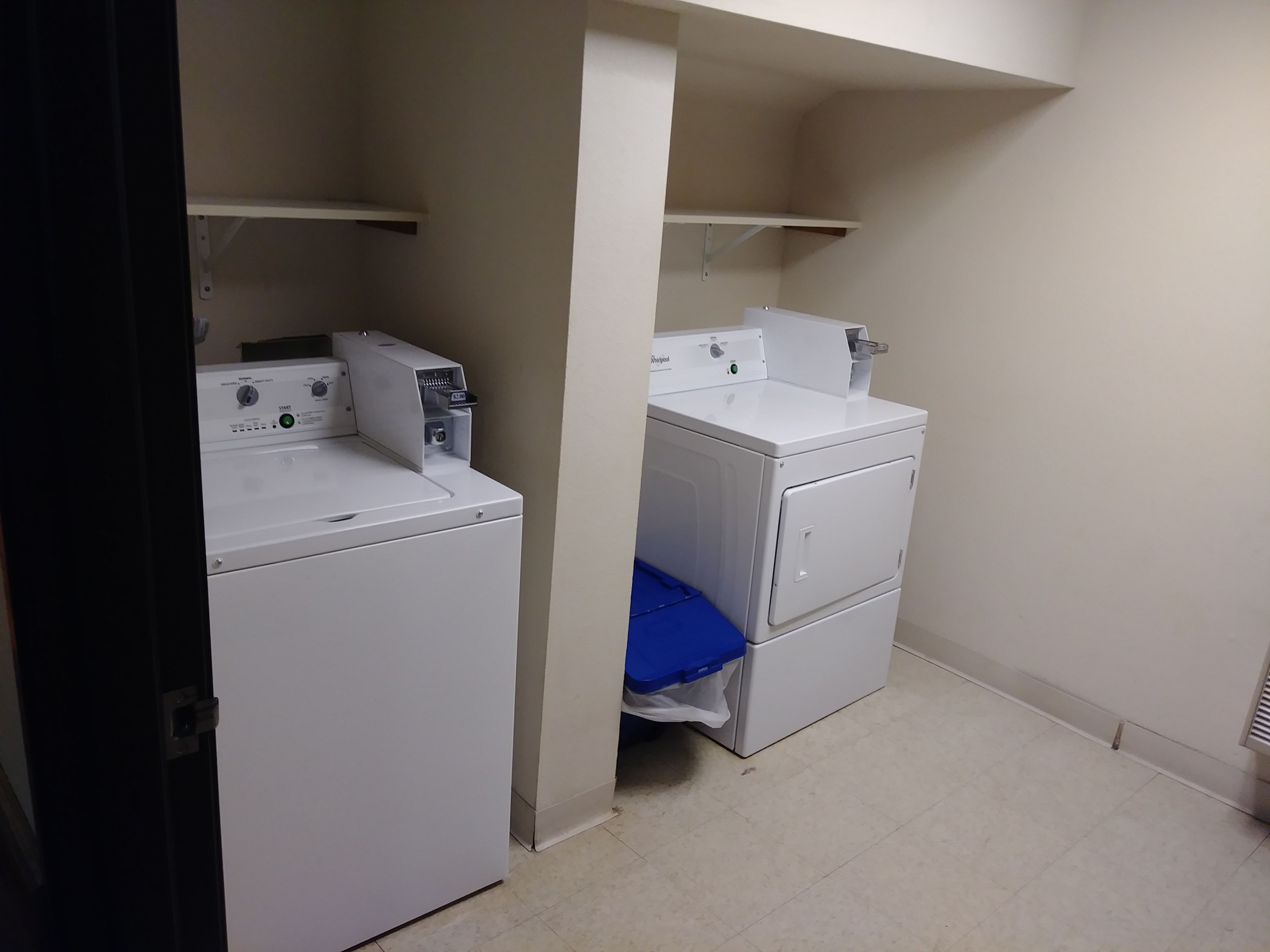 A laundry room with two stacked washers and dryers, a blue mat on the floor, and a shelf above the dryers.