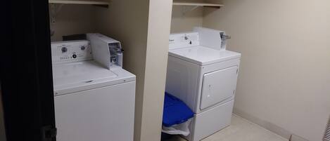 A laundry room with two stacked washers and dryers, a blue mat on the floor, and a shelf above the dryers.