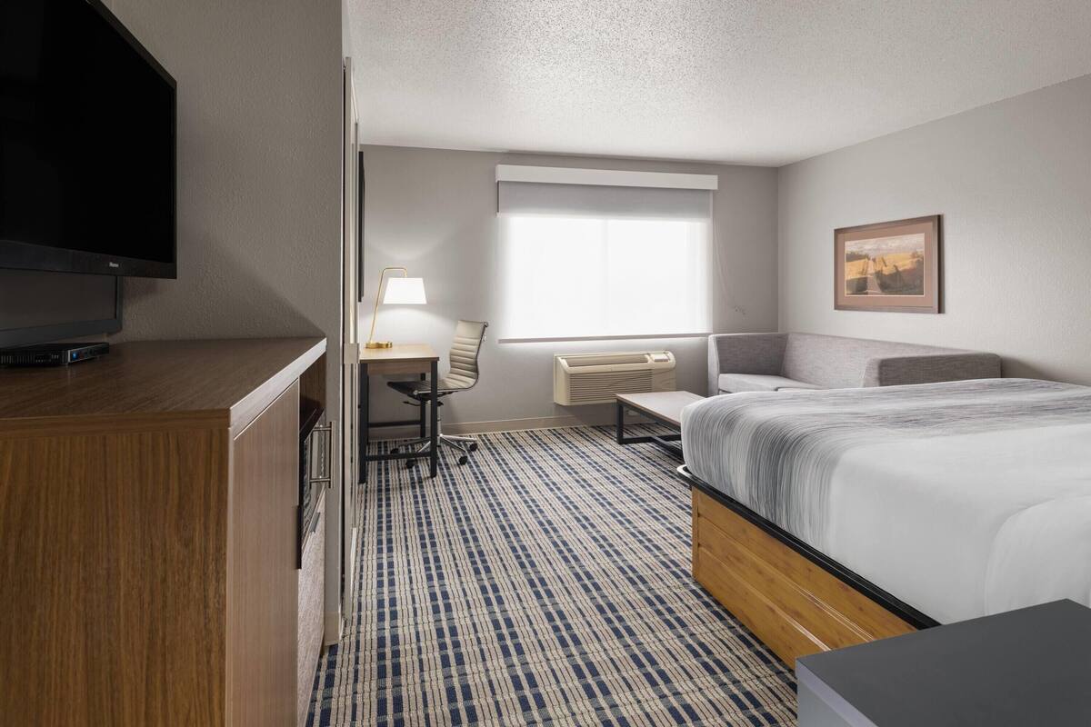 A hotel room with a bed, a desk with a chair, a television, and a window with a view.