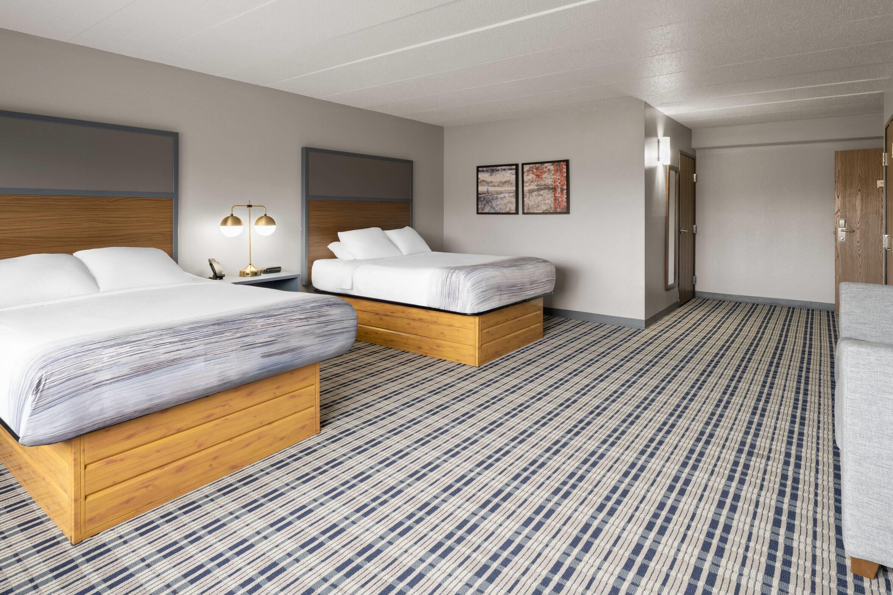 A hotel room with two beds, a nightstand, a lamp, and a door.