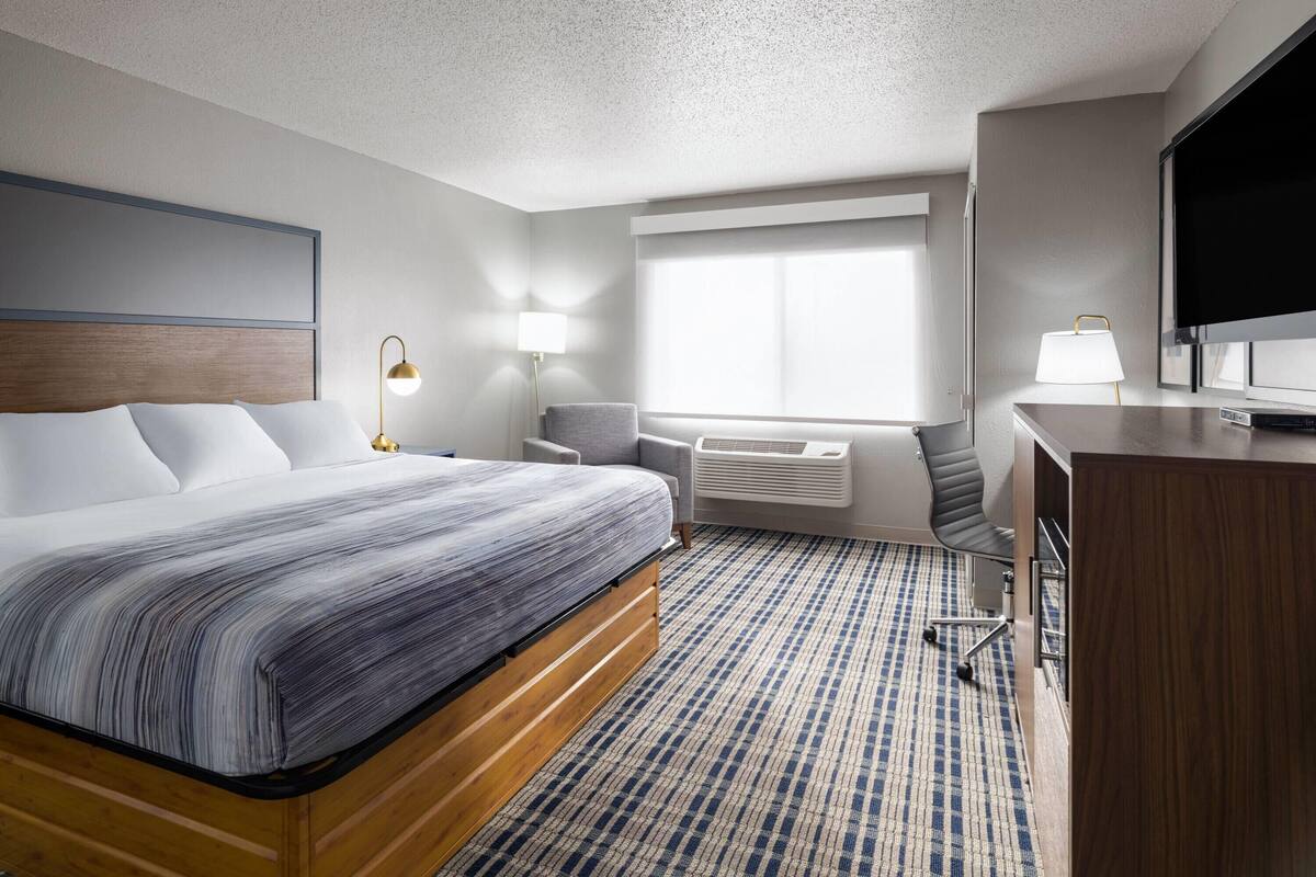A hotel room with a bed, a desk, a chair, a TV, and a window.