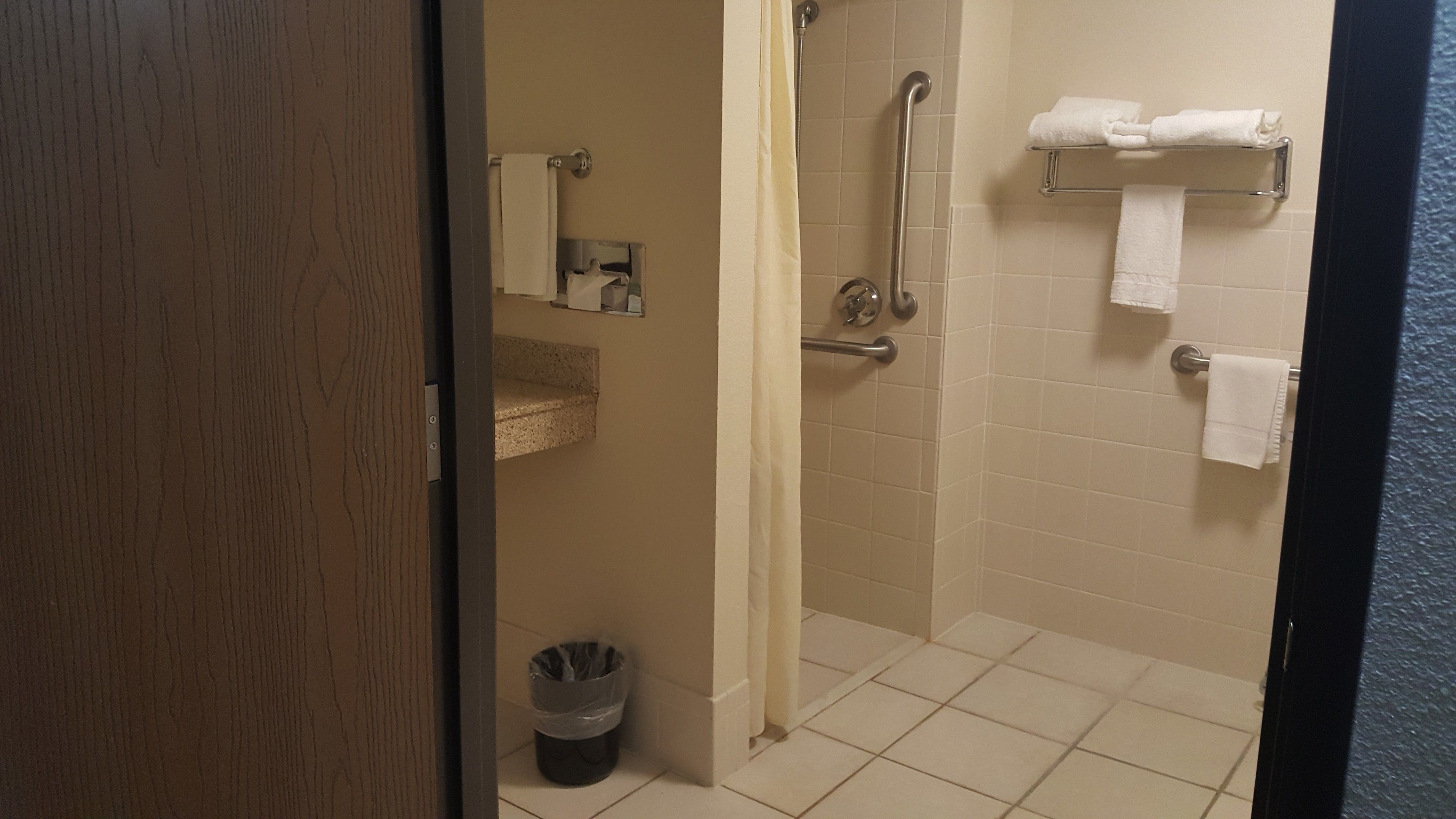 A bathroom with a shower, a toilet, a trash bin, and a towel rack with towels.