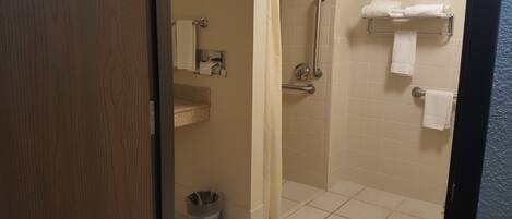 A bathroom with a shower, a toilet, a trash bin, and a towel rack with towels.