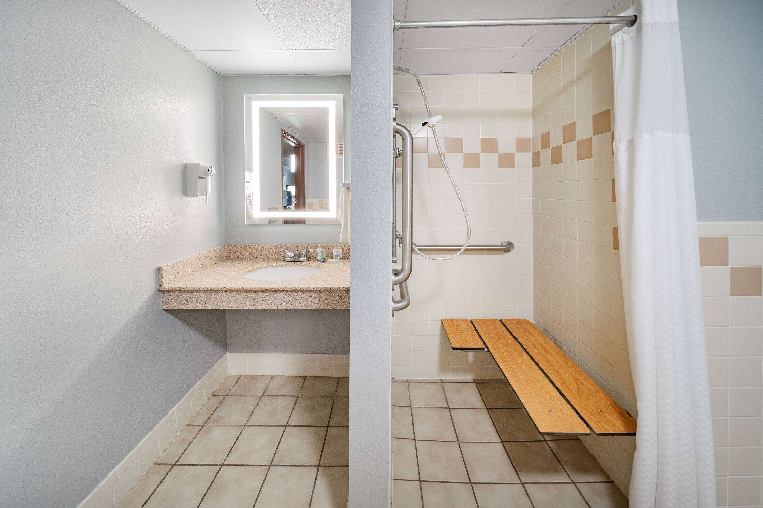 Ein Badezimmer mit Waschbecken, Spiegel, Dusche und Sitzbank.