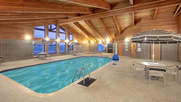 An indoor swimming pool with wooden beams, tiled walls, and a seating area with umbrellas. - AmericInn by Wyndham Sayre (Sayre)